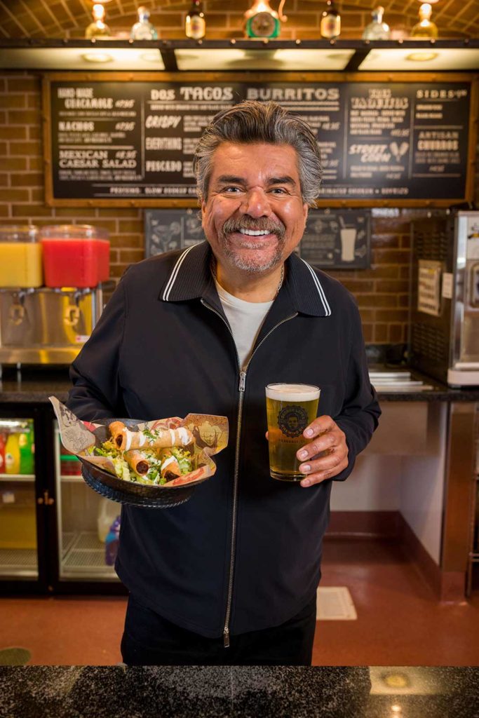 George Lopez holding a glass of beer and food